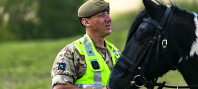 MOD personnel in hi-vis gilet talking to a horse rider